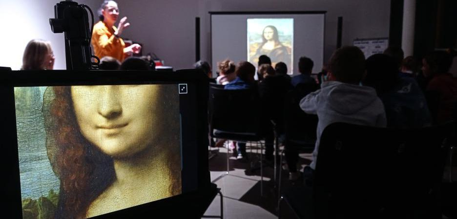 Animatrice et les elèves devant un ecran, sur le premier plan un tablette avec une photo de Mona Lisa