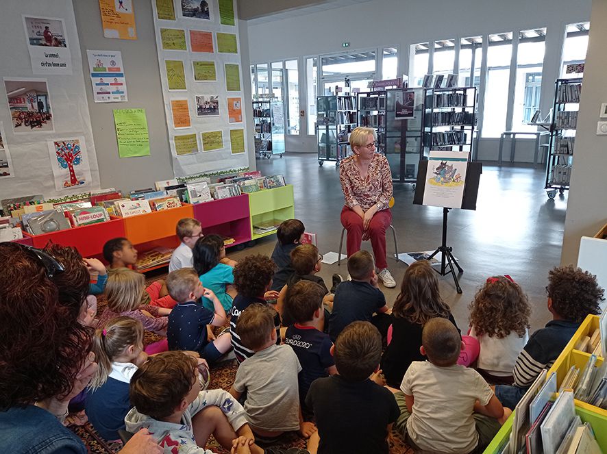 Une bibliothécaire lit un livre aux enfants assises devant elle.