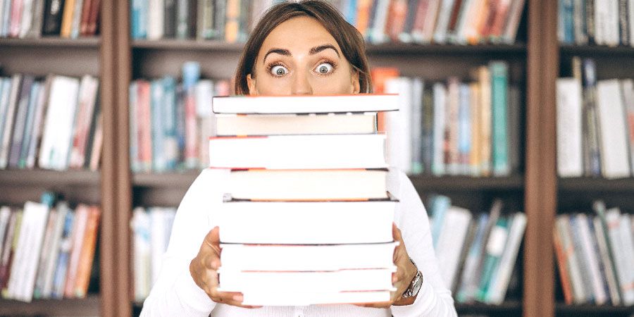 Une femme tient une pile de livres qui cache moitié de son visage.